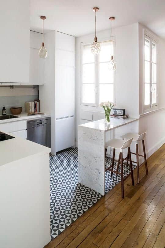 Modern small kitchen with minimalist white cabinetry, marble island, stainless steel appliances, and black-and-white geometric tiles.