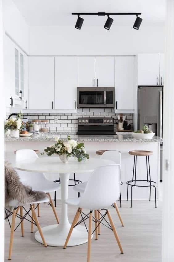Sleek modern kitchen with white cabinetry, granite countertop, central island, and round dining table, maximizing space and functionality.