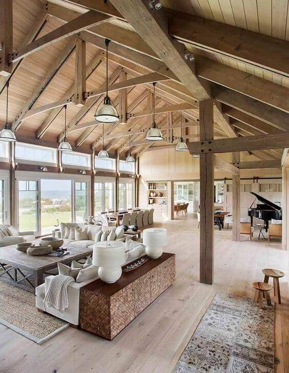 Spacious farmhouse interior with vaulted ceilings, large sectional sofa, reclaimed wood coffee table, and elegant piano, bathed in natural light.