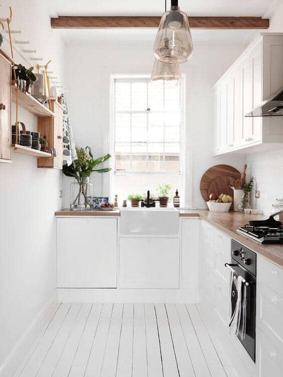 Bright, minimalist small kitchen features white walls, farmhouse sink, wooden countertops, and open shelving for storage solutions.