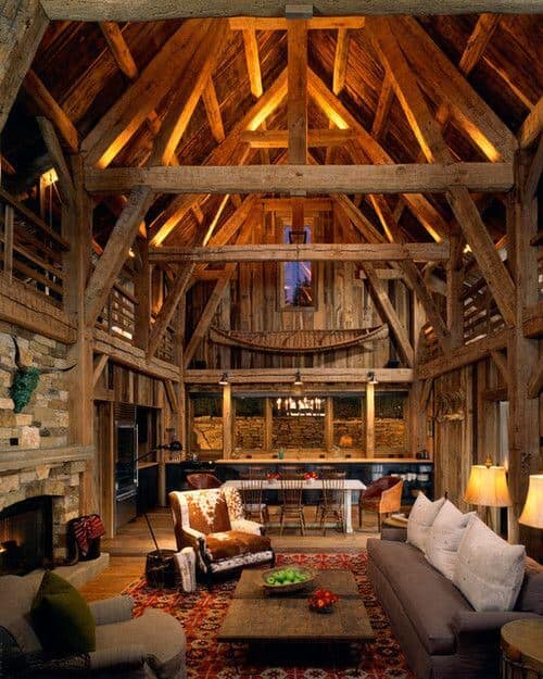 Cozy farmhouse interior featuring exposed wooden beams, a stone fireplace, and reclaimed wood accents. Earthy tones create a warm atmosphere.