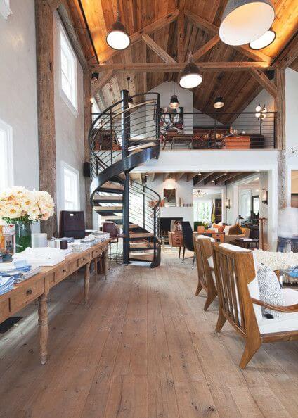 Spacious farmhouse interior with rustic and modern elements, featuring wide-plank hardwood floors, vaulted ceilings, and a spiral staircase.