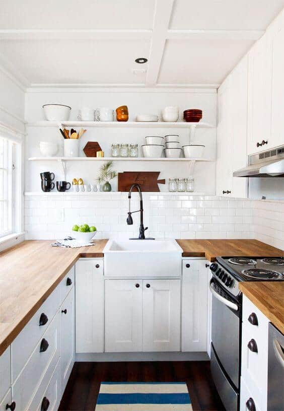 Farmhouse sink as a centerpiece in a small kitchen with white shaker cabinets, light wood countertops, and stainless steel appliances.