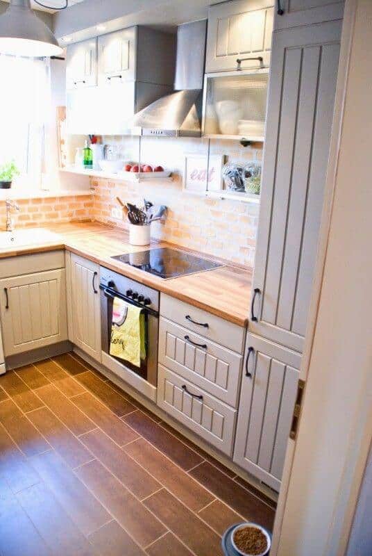 Compact small kitchen featuring light gray cabinetry, wooden countertop, and warm-toned backsplash. Optimized layout for functionality.