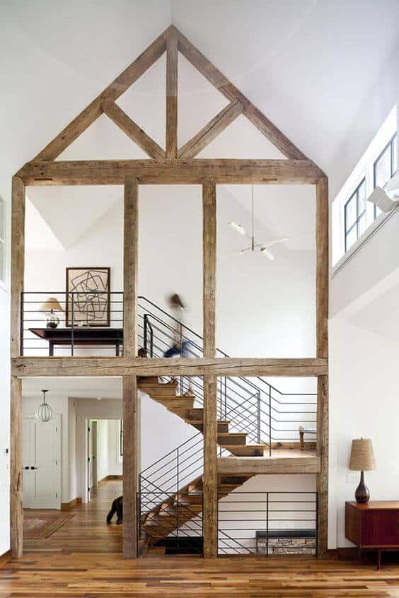 Modern farmhouse interior with a wooden frame, polished staircase, large windows, and cozy ambiance, blending rustic and contemporary styles.