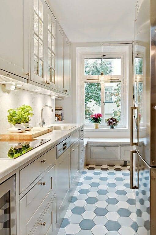 Modern small kitchen with soft gray cabinetry, white countertop, and hexagonal floor tiles. Natural light enhances space with potted plant areas.