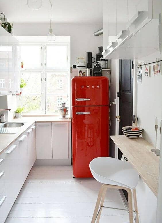 Modern small kitchen with white cabinetry, natural wood countertop, and a red retro refrigerator. Bright atmosphere with sleek seating and wooden floor.