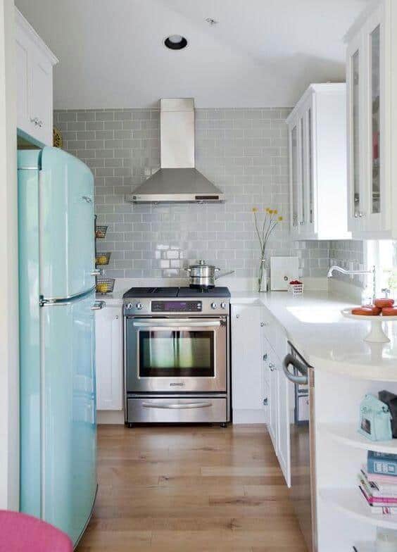 A compact kitchen with retro mint green refrigerator, stainless steel appliances, white cabinetry, light gray subway tile, and natural wood flooring.