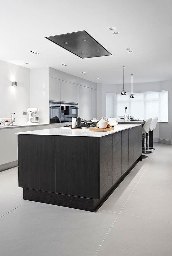 Modern kitchen with a large central island, white quartz countertop, dark wood cabinetry, and sleek grey tile flooring. Bright and airy with natural light.