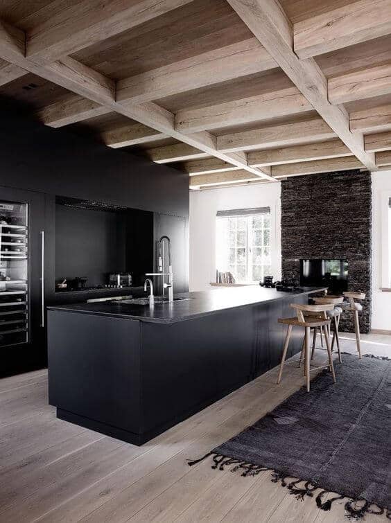 Sleek modern kitchen featuring a black island, matte cabinetry, wooden beams, and a stone wall, ideal for farmhouse interior design.