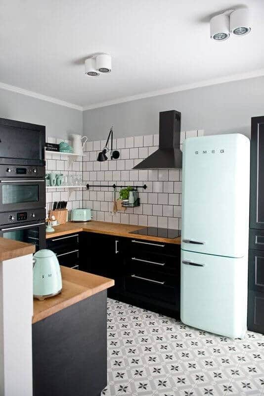 Modern L-shaped kitchen with sleek black cabinetry, light wood countertop, gas stovetop, mint green refrigerator, and decorative subway tiles.