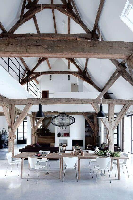 Spacious open concept dining area with reclaimed wood beams, polished concrete floor, and a large wooden table surrounded by white chairs.