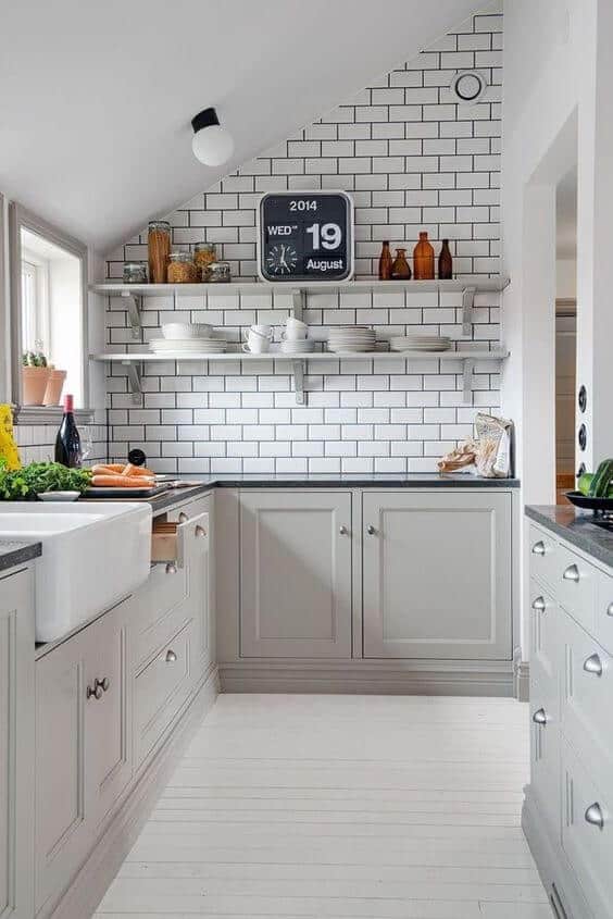 Elegant small kitchen with grey cabinets, dark granite countertop, farmhouse sink, and white subway tile backsplash. Features open shelving and light wood flooring.