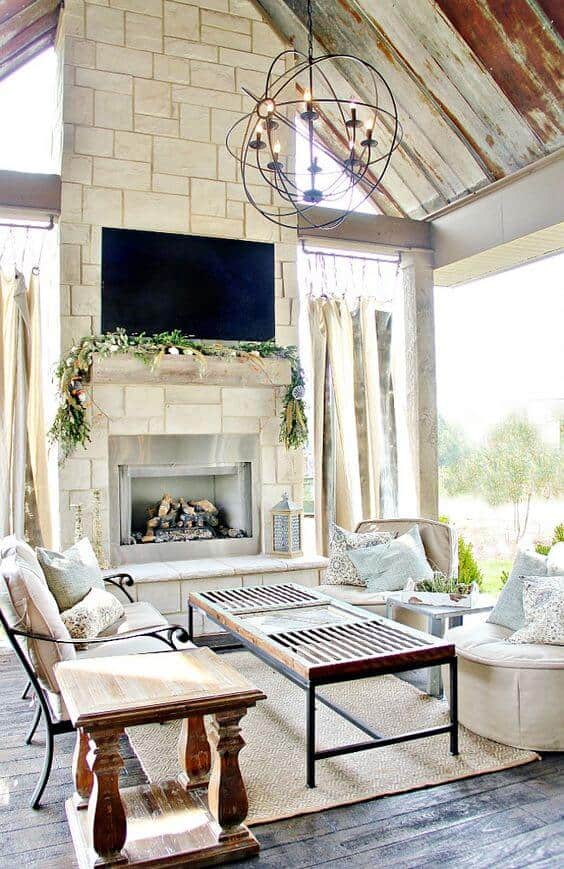 Cozy living room with a stone fireplace, vaulted wooden beam ceiling, plush seating, and natural light from large windows.