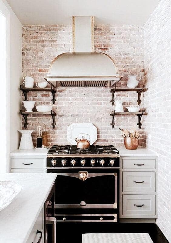 Modern small kitchen featuring a black gas range with brass accents, open dark wood shelving, and gray cabinetry, maximizing space with style.