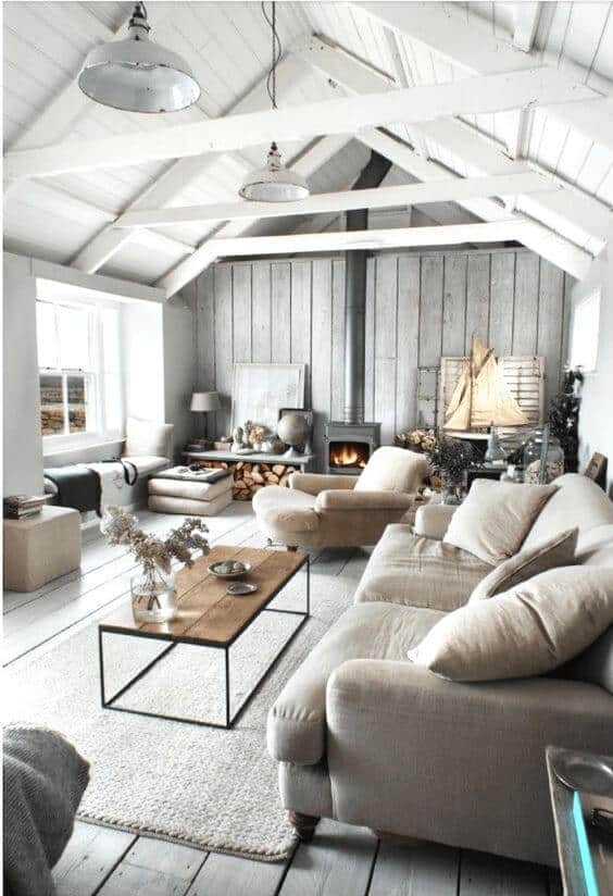 Spacious farmhouse interior with vaulted ceiling and exposed beams. Soft beige sectional, rustic coffee table, and natural decor create a cozy atmosphere.