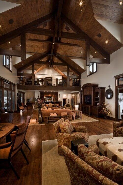 Rustic living room with exposed wooden beams, high vaulted ceiling, plush sofas, and natural light from large windows. Cozy and stylish decor.