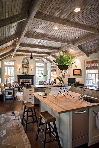 Spacious farmhouse kitchen with a natural wood island, exposed beams, large windows, and cozy decor, blending modern and rustic styles.