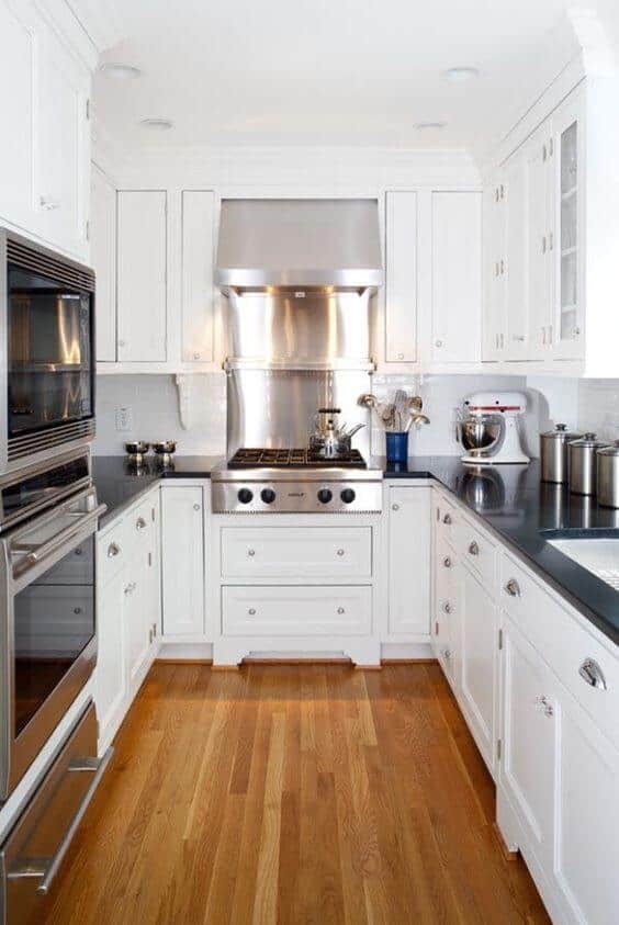 U-shaped small kitchen with white cabinetry, polished chrome hardware, dark granite countertops, and a central island with a stainless steel stove.