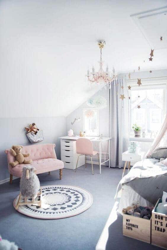 Pastel kids' bedroom with soft blue walls, plush gray carpet, light pink loveseat, and white desk, illuminated by natural light.