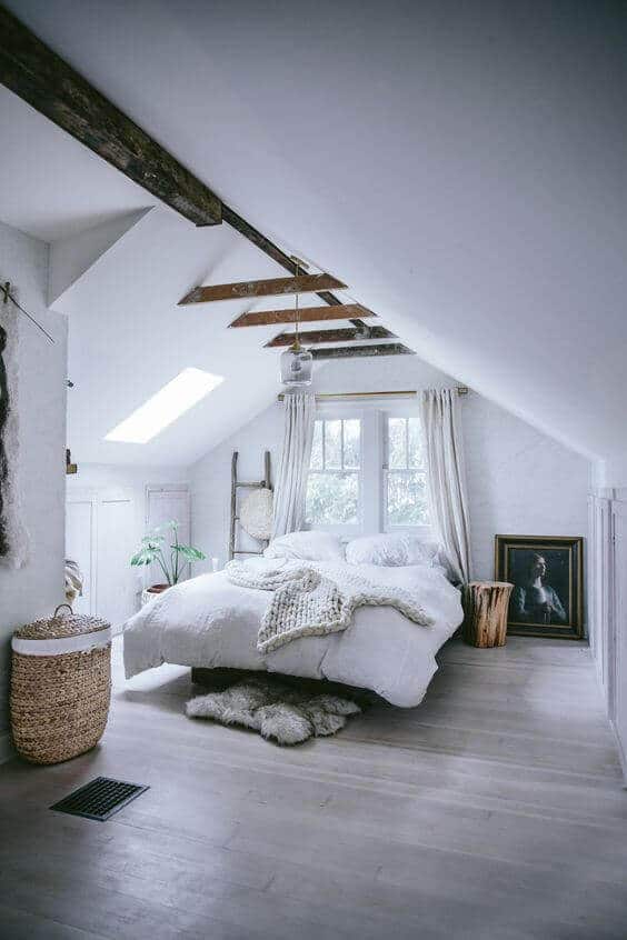 Attic bedroom with sloped ceilings, skylight, queen bed, textured duvet, warm wood flooring, and vintage portrait, exuding rustic charm.