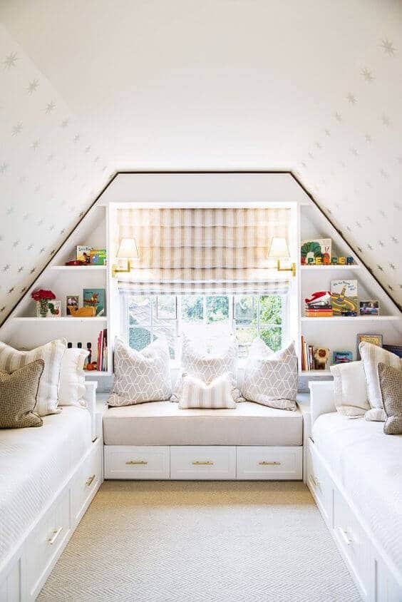 Cozy attic room with twin beds, integrated storage, and a plush central bench. Soft white walls, star patterns, and natural light enhance the inviting atmosphere.