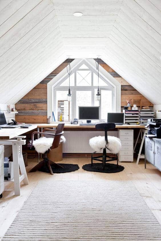 Bright attic office with slanted shiplap walls, two minimalist desks, and modern lighting. Natural light floods in, enhancing productivity.