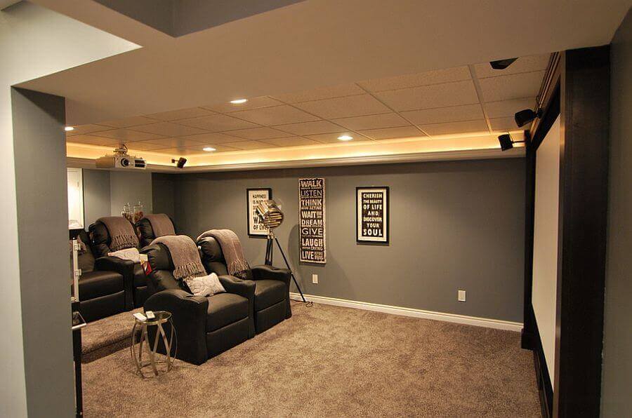 Plush reclining seats in a cozy basement playroom, soft carpet, gray walls, projector screen, and adjustable LED lighting. Ideal for kids.