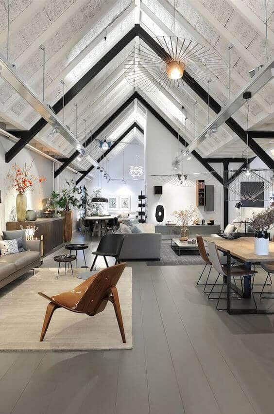 Spacious modern attic room with vaulted ceiling, neutral sectional sofa, wooden coffee table, and natural light from large windows.