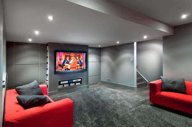 Contemporary basement playroom featuring minimalist design, gray palette, two red sofas, a wall-mounted TV, and a cozy black rug.