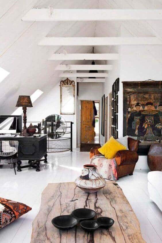 Vaulted attic space features exposed beams, a rustic wood coffee table, black ceramic bowls, and a leather armchair with a yellow pillow.