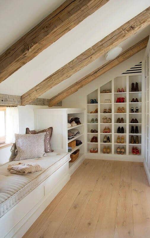 Cozy attic nook with a built-in window seat, plush fabrics, warm wooden beams, and organized shoe storage for optimal space planning.