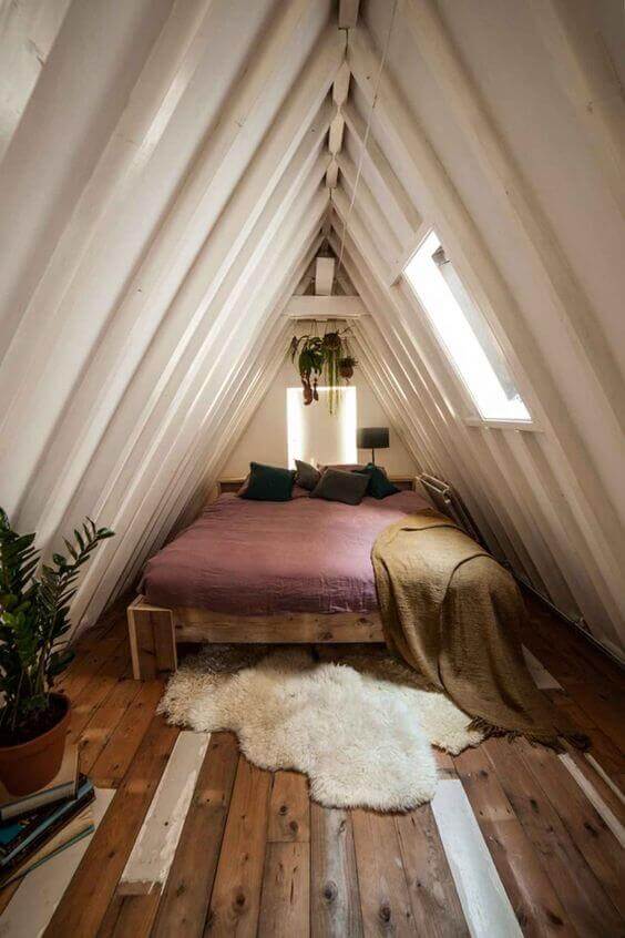 Attic bedroom with sloped roof, wooden beams, queen bed in mauve, cozy throw pillows, faux fur rug, and potted greenery for a serene feel.