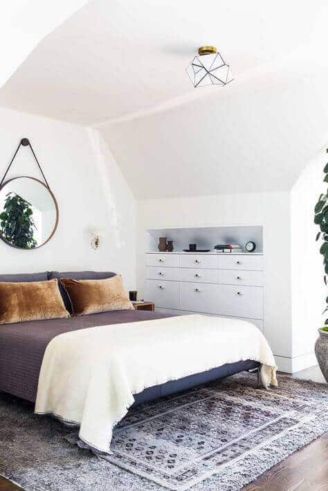 Cozy attic bedroom featuring a queen-sized bed with a dark gray duvet, earthy pillows, and natural light enhancing the airy feel.