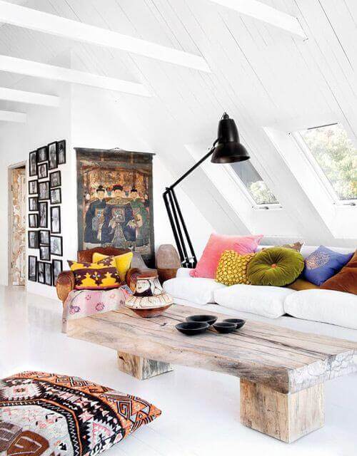 Bright, open attic space with high beamed ceilings, rustic wooden coffee table, colorful pillows, and a gallery wall, perfect for relaxation.