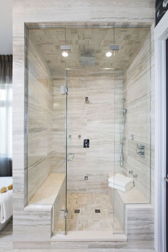 Modern spa bathroom featuring a glass shower enclosure, natural stone tiles, and a built-in bench for comfort. Soft lighting enhances the tranquil atmosphere.