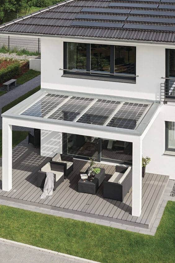 Sleek modern patio with a solar panel rooftop, wooden deck, modular seating, and greenery, blending with the lawn in a sunny layout.