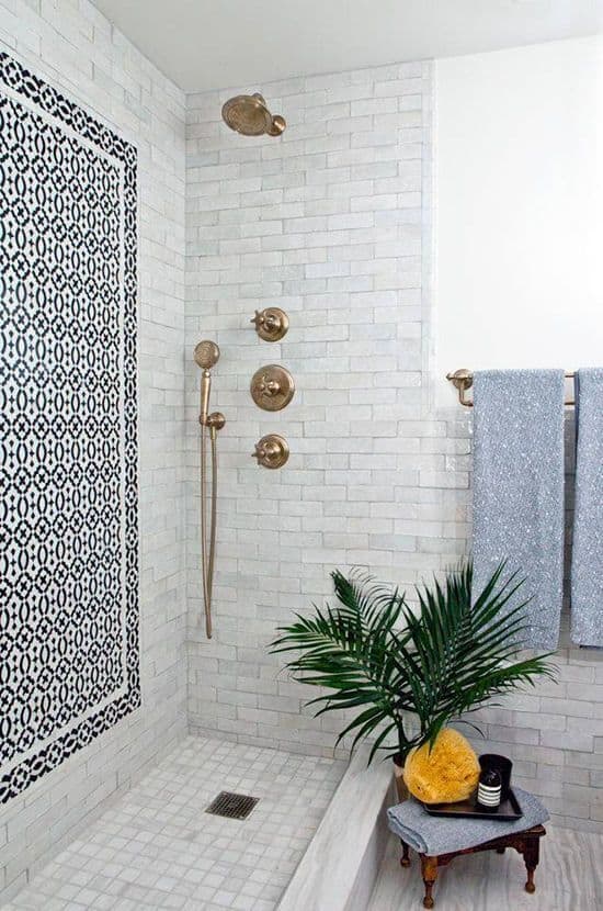 Modern spa bathroom featuring large white subway tiles, a black and white patterned accent wall, brass fixtures, and lush greenery.