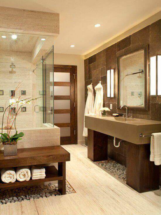 Spa bathroom with minimalist design, dark slate walls, light stone flooring, glass walk-in shower, dual-sink vanity, and ambient lighting.
