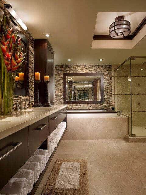 Spacious spa bathroom with natural stone flooring, dark wood cabinetry, stylish lighting, a large mirror, and a glass-enclosed shower.