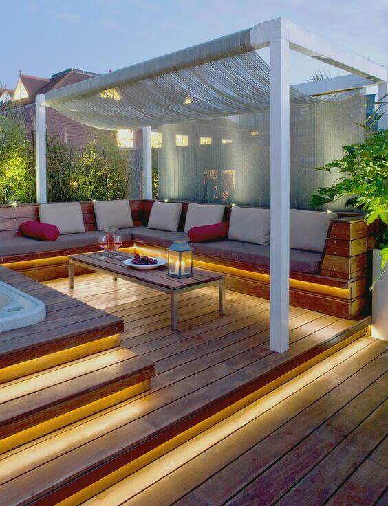 Cozy outdoor seating area with durable wooden furniture, light upholstery, and red cushions under a stylish canopy, perfect for relaxation.