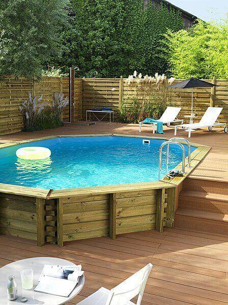 27 Above Ground Pool Landscaping Creative Ideas 3 Oval above ground pool with wooden deck, surrounded by greenery, two lounge chairs, and a small table for relaxation.