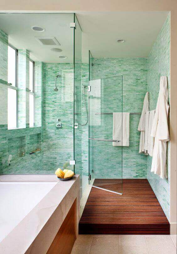 Luxurious spa bathroom featuring a glass shower enclosure, green mosaic tiles, rainfall showerhead, and warm wood accents for a calming vibe.