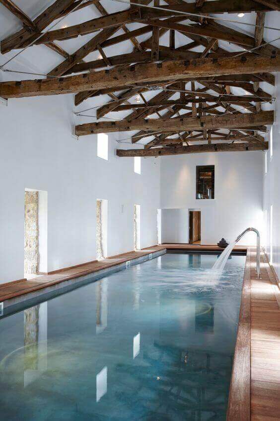 Sleek indoor swim spa with natural wood decking, large windows for sunlight, and a minimalist design, ideal for relaxation.