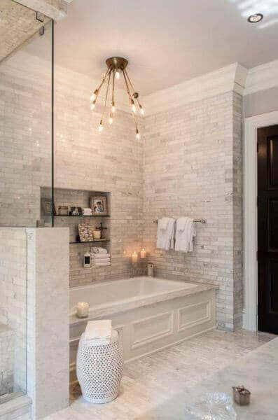Serene spa bathroom featuring light stone tiles, a rectangular tub, glass shower enclosure, and a modern pendant light for a calming vibe.