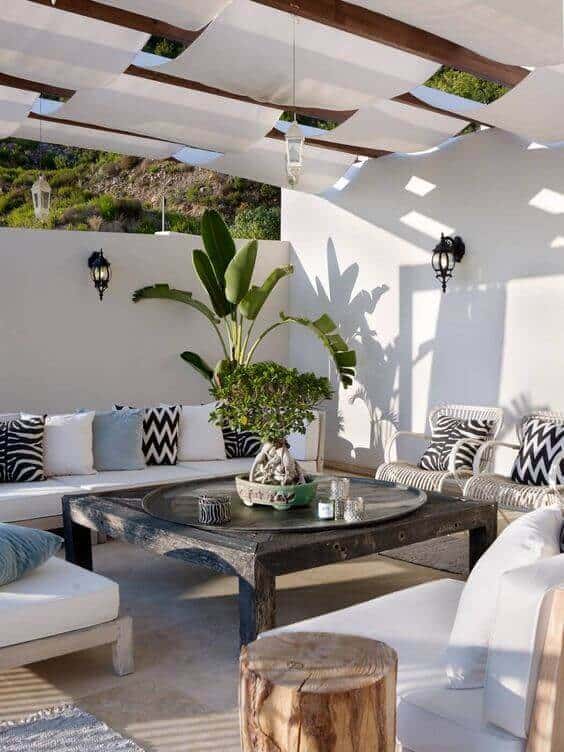 Stylish outdoor seating area under a fabric-draped pergola, featuring a U-shaped sofa, round wooden coffee table, and potted plant.