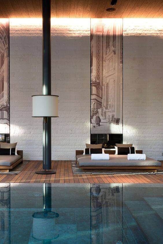 Modern indoor swim spa retreat with sleek design, serene atmosphere, lounge beds on wooden decking, and a tranquil swimming pool.