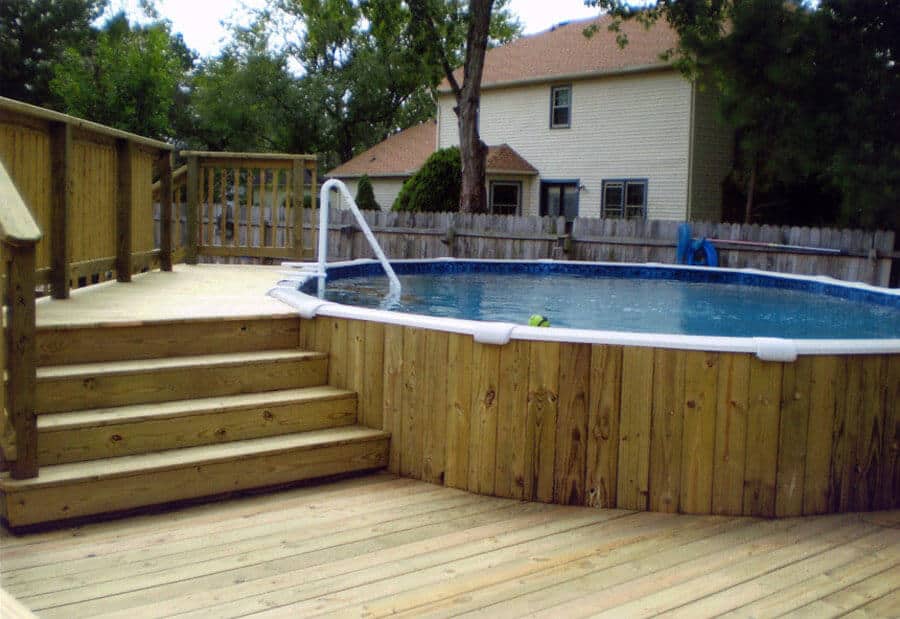 27 Above Ground Pool Landscaping Creative Ideas 27 Circular above ground pool with wooden deck, surrounded by trees and fencing, creating a serene backyard space for leisure.