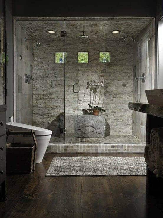 Modern spa bathroom featuring a glass shower enclosure, textured stone walls, and natural stone tiles, creating a serene atmosphere.