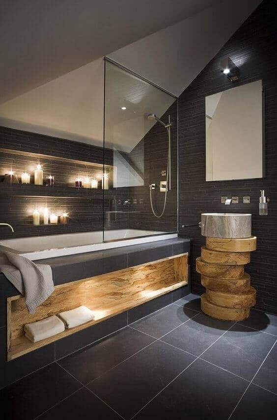 Modern spa bathroom featuring a glass-enclosed shower, sleek bathtub, dark textured tiles, and warm candlelit shelves for a calming vibe.